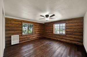 Spare room with a textured ceiling, dark hardwood floors, ceiling fan, and log walls