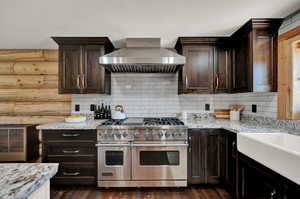 Kitchen with double oven range, wall chimney range hood, dark real hard wood flooring, and backsplash