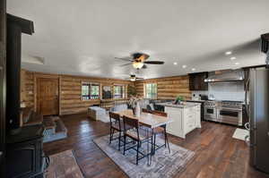 Kitchen with stainless steel appliances, log walls, wall chimney exhaust hood, tasteful backsplash, and ceiling fan