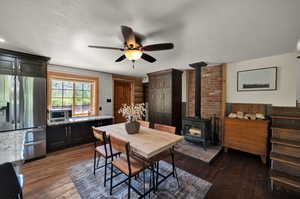 Dining space with brick wall, dark hardwood floors, ceiling fan, and a wood stove