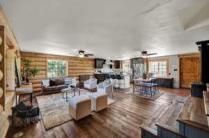 Living room with a textured ceiling, ceiling fan, log walls, and wood-type flooring