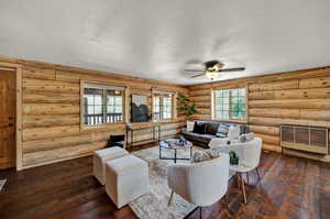 Living room with rustic walls, ceiling fan, and dark hardwood floors