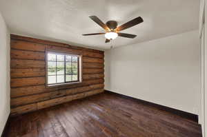 Empty room featuring a textured ceiling, dark hardwood  flooring, ceiling fan, and log walls