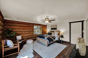 Bedroom featuring rustic walls, dark hardwood floors, and ceiling fan