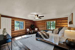 Bedroom with ceiling fan, a textured ceiling, hardwood flooring, and rustic walls