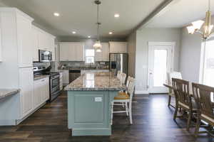 Kitchen featuring dark hardwood / wood-style floors, pendant lighting, a center island, white cabinetry, and appliances with stainless steel finishes