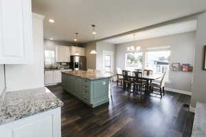 Kitchen featuring white cabinetry, stainless steel fridge, a center island, green cabinets, and pendant lighting