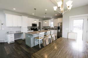 Kitchen with a center island, appliances with stainless steel finishes, white cabinets, light stone counters, and a kitchen bar