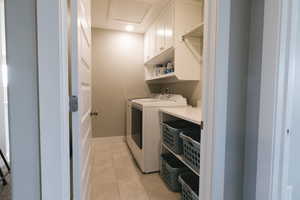 Laundry room with cabinets, light tile floors, and washing machine and clothes dryer