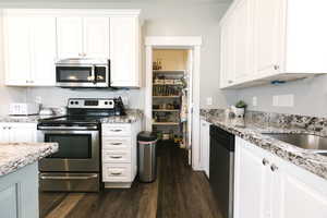 Kitchen featuring appliances with stainless steel finishes, white cabinets, dark hardwood / wood-style floors, and light stone countertops