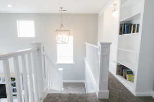 Stairway with a chandelier and dark carpet