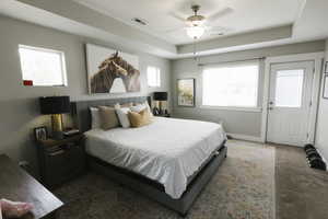 Carpeted bedroom featuring ceiling fan and a tray ceiling