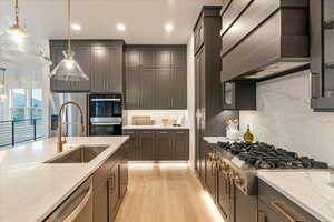 Kitchen featuring backsplash, hanging light fixtures, light stone countertops, and sink