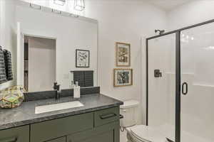 Bathroom featuring a shower with shower door, vanity, and toilet