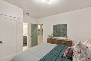 Bedroom featuring light carpet, a textured ceiling, and connected bathroom