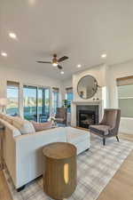 Living room with a tiled fireplace, light wood-type flooring, and ceiling fan