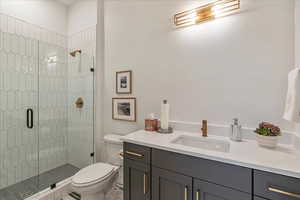 Bathroom featuring a shower with shower door, toilet, and vanity