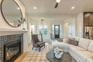 Living room with ceiling fan, a tile fireplace, and light hardwood / wood-style flooring