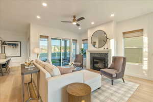 Living room featuring ceiling fan, a tiled fireplace, and light hardwood / wood-style floors