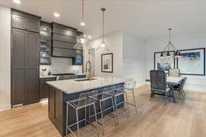 Kitchen with light wood-type flooring, an island with sink, light stone counters, sink, and custom exhaust hood