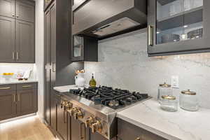 Kitchen featuring light hardwood / wood-style floors, light stone counters, backsplash, range, and wall chimney exhaust hood