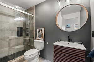 Tiled shower combination, medium brown slatted vanity with mirror, toilet with wood type flooring