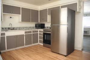 Kitchen with sink, a wall unit AC, light wood-type flooring, and stainless steel appliances