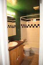 Full bathroom with vanity with extensive cabinet space, tile flooring, toilet, and tiled shower / bath combo