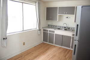 Kitchen with gray cabinetry, sink, white fridge, and light wood-type flooring