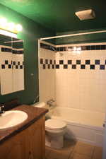 Full bathroom with tiled shower / bath combo, vanity, toilet, and tile floors