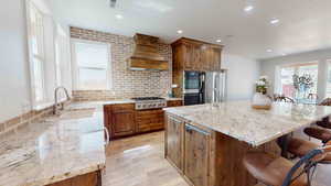 Kitchen with light hardwood / wood-style flooring, custom exhaust hood, a center island, appliances with stainless steel finishes, and a breakfast bar