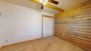 Unfurnished room featuring ceiling fan, carpet flooring, and rustic walls