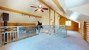 Additional living space featuring carpet flooring, rustic walls, lofted ceiling with beams, and ceiling fan