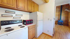 Kitchen featuring white appliances, light hardwood / wood-style floors, a wood stove, and log walls