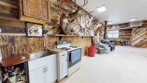 Kitchen featuring white cabinetry, sink, wooden walls, and white range with electric stovetop