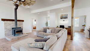 Living room featuring ceiling fan, a wood stove, and light hardwood / wood-style floors