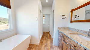 Bathroom with a bath to relax in, vanity with extensive cabinet space, and hardwood / wood-style flooring