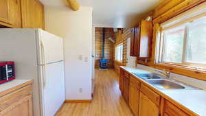 Kitchen with light hardwood / wood-style floors, a wood stove, sink, rustic walls, and white fridge