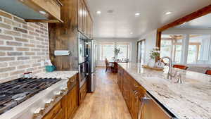 Kitchen with light hardwood / wood-style flooring, stainless steel appliances, premium range hood, light stone counters, and sink