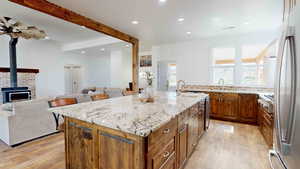 Kitchen featuring ceiling fan, light wood-type flooring, light stone counters, a wood stove, and a kitchen island with sink