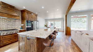 Kitchen with stainless steel appliances, a center island with sink, light hardwood / wood-style flooring, and light stone counters