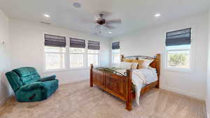 Bedroom with light colored carpet, ceiling fan, and multiple windows