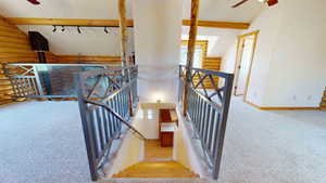 Staircase featuring ceiling fan, vaulted ceiling with beams, carpet flooring, track lighting, and rustic walls