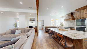 Kitchen with an island with sink, a wealth of natural light, wood-type flooring, and custom range hood