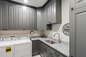 Clothes washing area featuring washing machine and dryer, sink, and cabinets