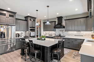 Kitchen with stainless steel appliances, light wood-type flooring, custom range hood, a kitchen island, and backsplash