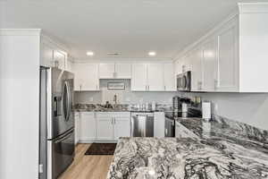 Kitchen featuring sink, stainless steel appliances, light hardwood / wood-style flooring, and white cabinetry