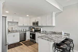 Kitchen with kitchen peninsula, stainless steel appliances, light wood-type flooring, a breakfast bar area, and white cabinetry