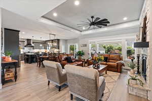 Living room featuring ceiling fan, light hardwood / wood-style floors, a tray ceiling, and a fireplace