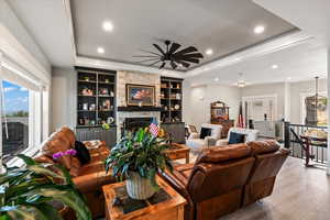 Living room with a fireplace, ceiling fan, a tray ceiling, hardwood / wood-style floors, and built in shelves